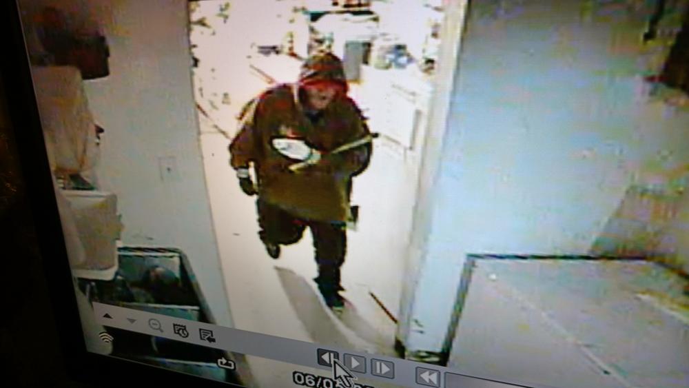The suspect in the brown jacket walking through the building.