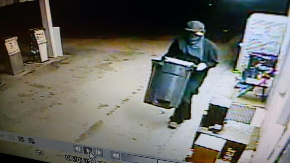 The suspect in the black jacket walking outside carrying a trash can.
